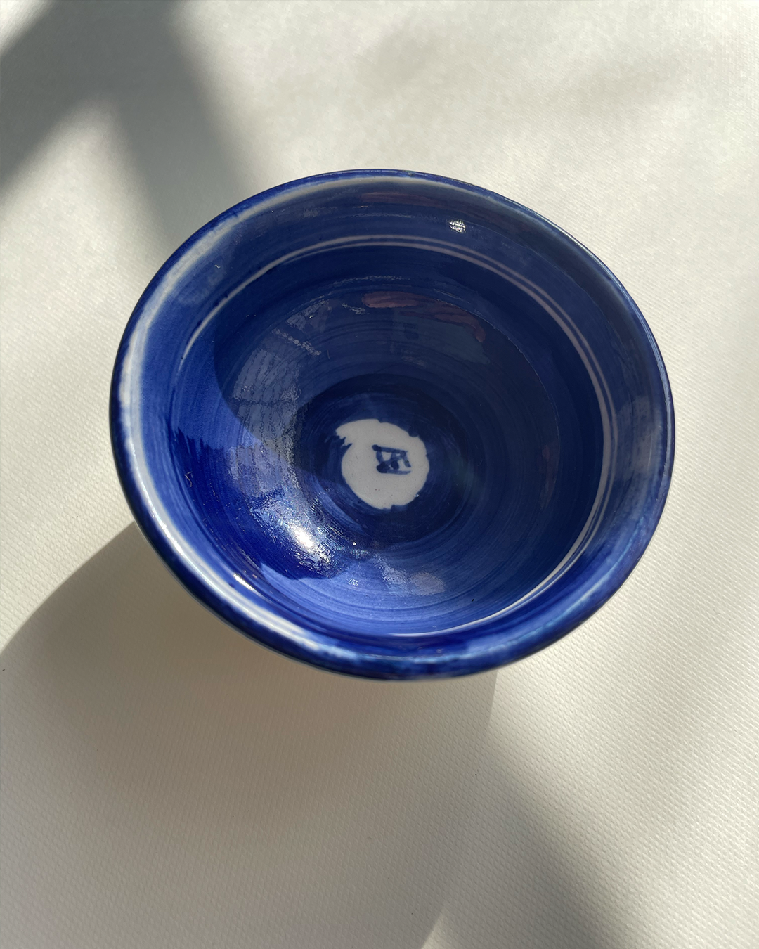 Mini bowl de cerámica, vista cenital, diseño del logo de Ene Ediciones, color blanco con azul.